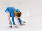 Cute young girl practicing figure skating on indoor ice skating rink.